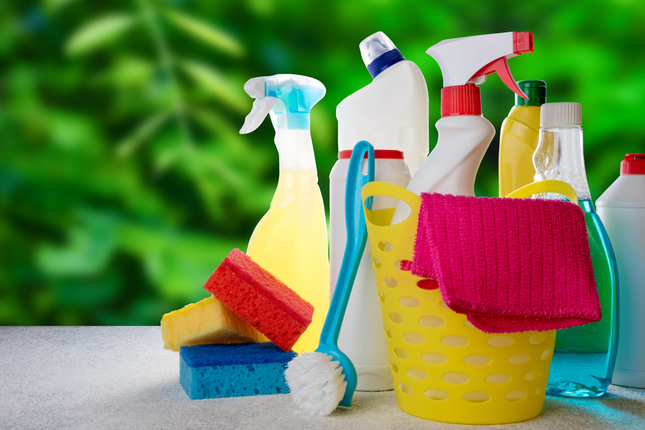 Basket with cleaning tools and products on blurry nature backgro